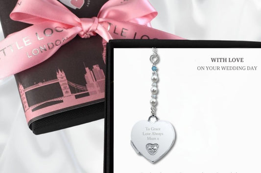 Sterling silver opening heart locket with tiny diamante engraved with text of your choice. Suspended from a string of white pearls and crystals and finished with a tiny blue crystal as a something blue. Shown in gift box with optional skyline wrap and pink branded ribbon in background.