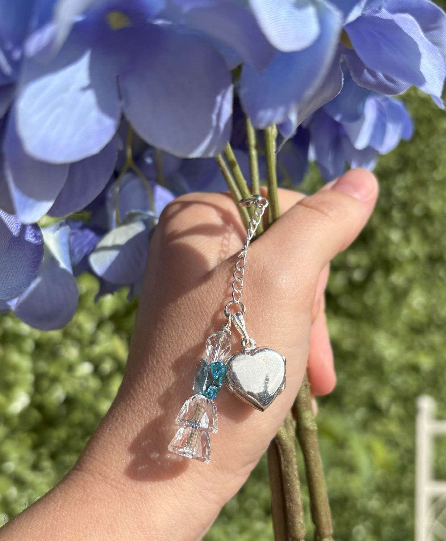 A sterling silver and crystal bouquet charm including a heart shaped locket. All crystal is highest quality and the angel's wing are blue as a nod to the something blue tradition. Suspended from a sterling silver chain and fastened to the bouquet via a lobster clasp.