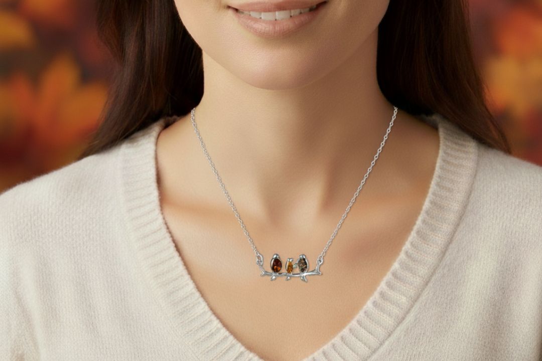 Sterling silver connector necklace showing three birds on a branch. The birds are inlaid with three types of amber - honey, cognac and olive. Shown worn.