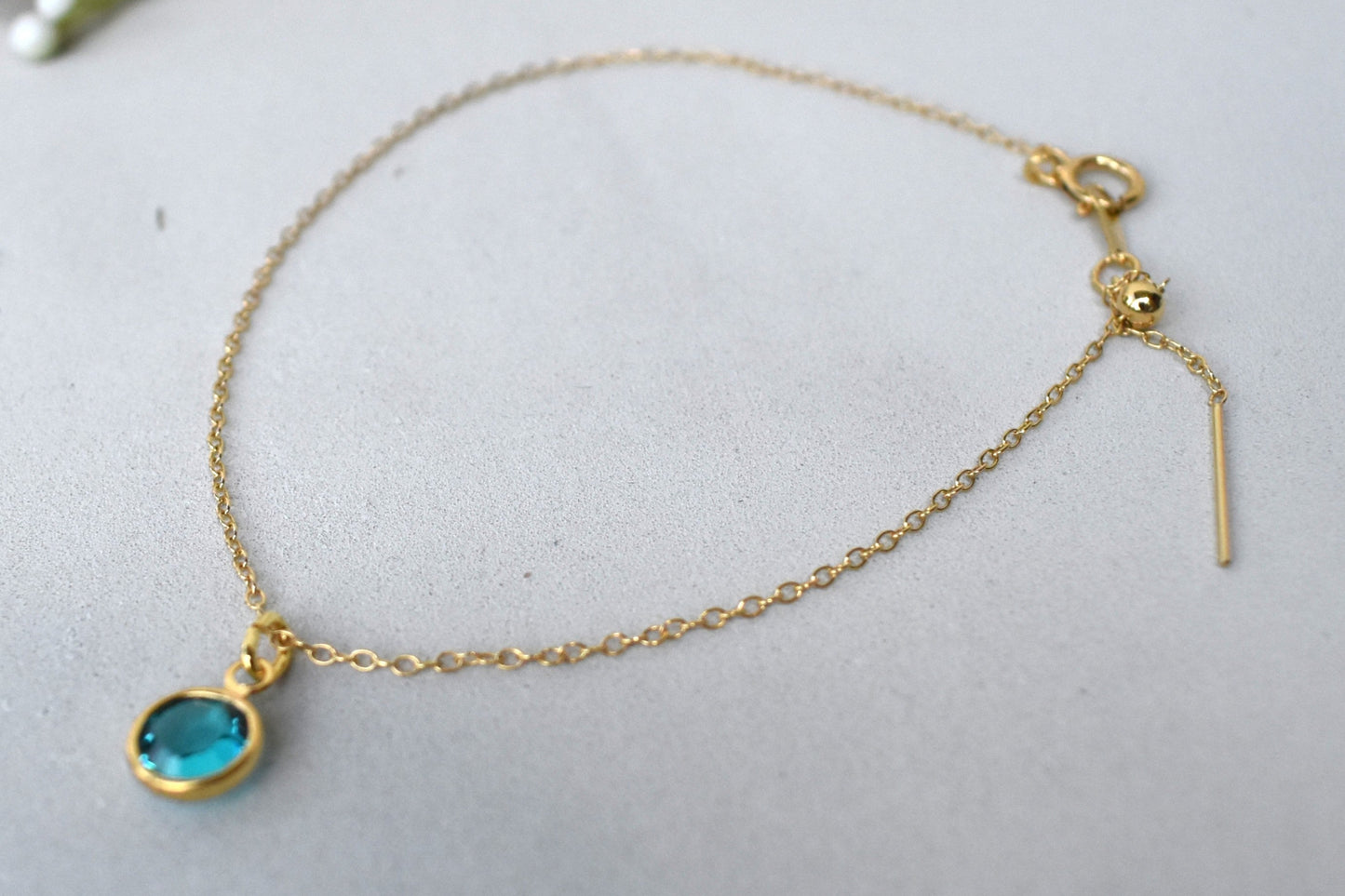 A gold filled chain is threaded through a bead to make this delicate bracelet adjustable. Finished with a birthstone of your choice, ths bracelet is the perfect summer accessory.