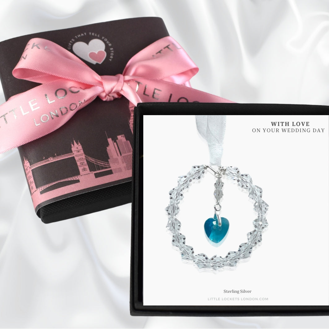 A circle of highest quality Austrian crystals surround an Austrian crystal blue heart. Suspended from white ribbon. A pretty something blue bouquet charm, shown in gift box with optional gift wrap inthe background