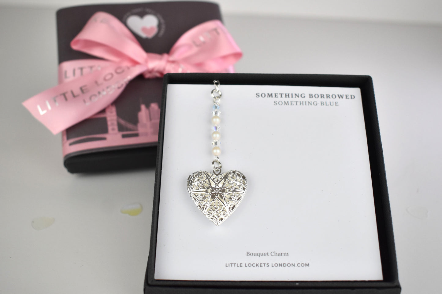 Our handmade wedding bouquet memorial charm has a slver plated filigree locket suspended from a string of high quality crystals and glass pearls and finished with a tiny blue bead as your something blue. Shown mounted on card in a branded gift box with wording of your choice. In the background is the optional upgraded gift wrap.