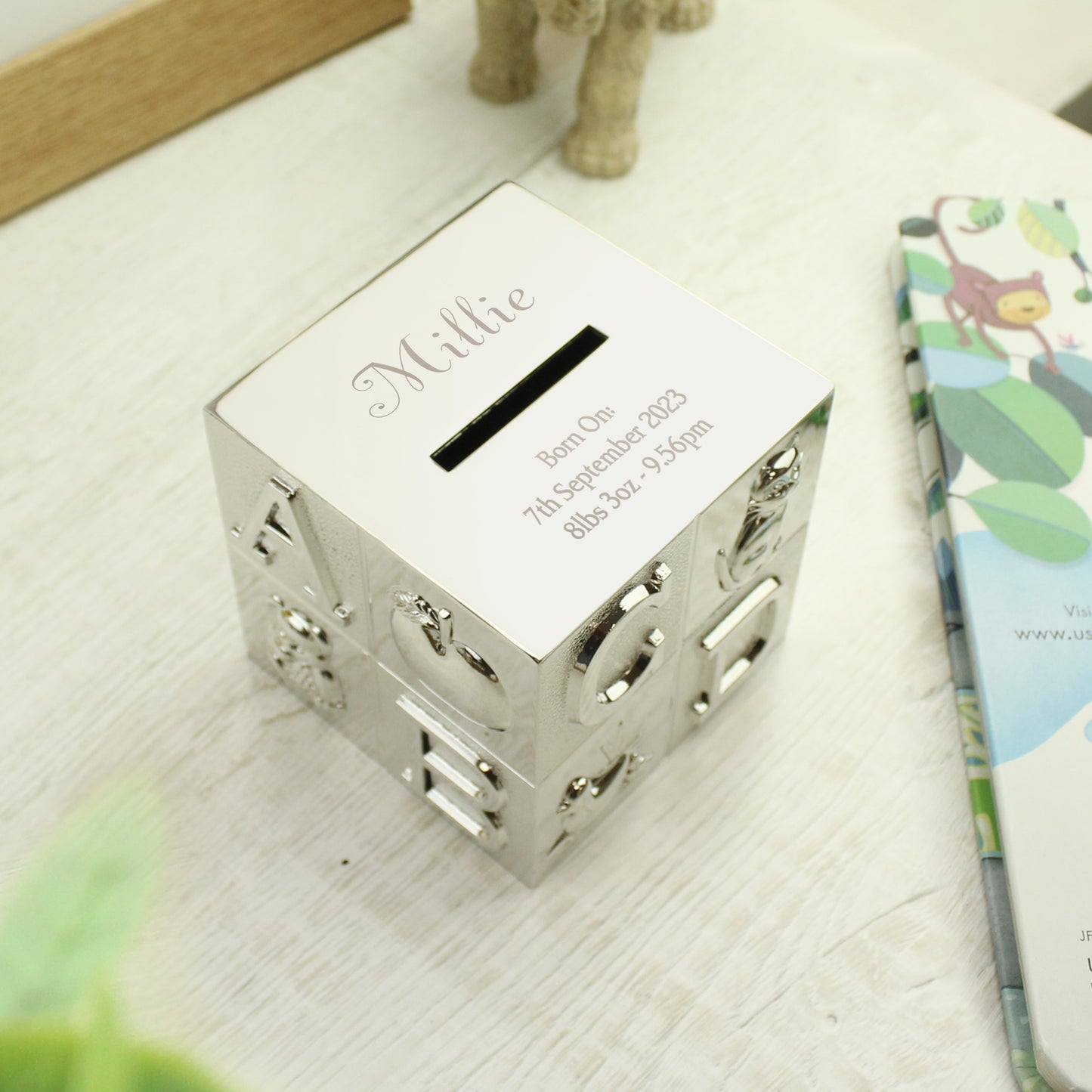 silver plated child's ABC money box. The child's name is engraved above the money slot in a script font. Beneath the money slot, there is room for three lines of text for your own message.