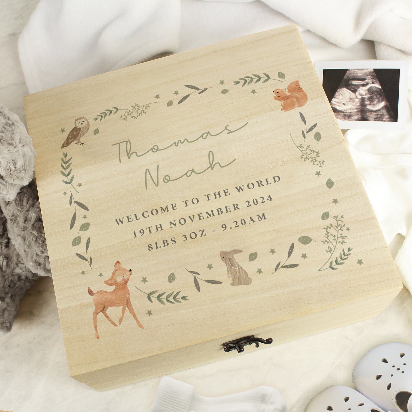 A wooden box with woodland animal and leaves forming a square. Within the square is five lines of personalised text, the first two in script font and the remaining three in block capitals. Fastened with a metal clasp.