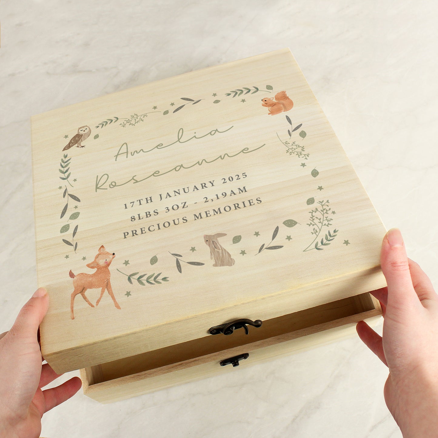 A wooden box with woodland animal and leaves forming a square. Within the square is five lines of personalised text, the first two in script font and the remaining three in block capitals. Fastened with a metal clasp.