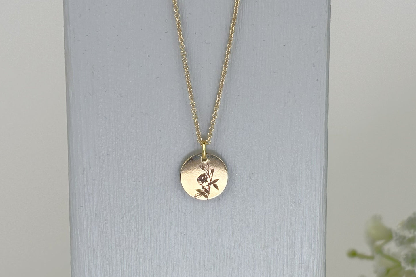 delicate Gold Filled Birth Flower Pendant. Crafted on an 11mm coin pendant, this simple piece is engraved with the intricate design of birth flowers on the front side and on the reverse side features a hidden personalised engraving, making it truly unique.