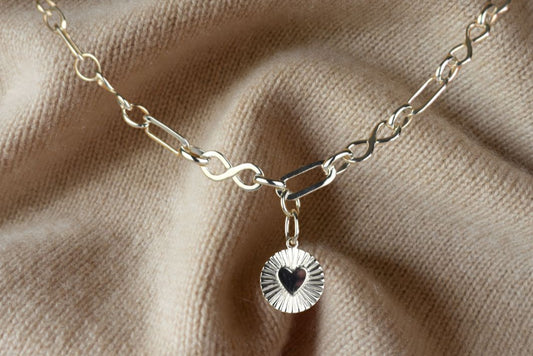 Sterling Silver Handmade Flat Link Infinity Necklace featuring a Heart Rays Pendant. Showcases flat oval and infinity links and features a Sterling Silver Sunburst Heart Rays charm pendant surrounded by an intricate sun rays design