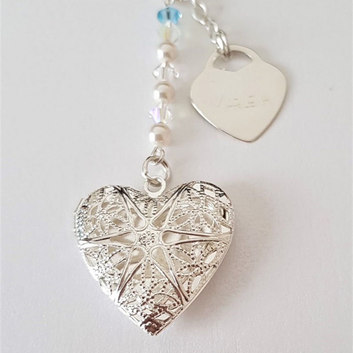 close up of wedding bouquet memorial charm. Showing filigree heart, glass pearls and crystals, a tiny something blue crystal and a sterling silver heart engraved with your choice of text.