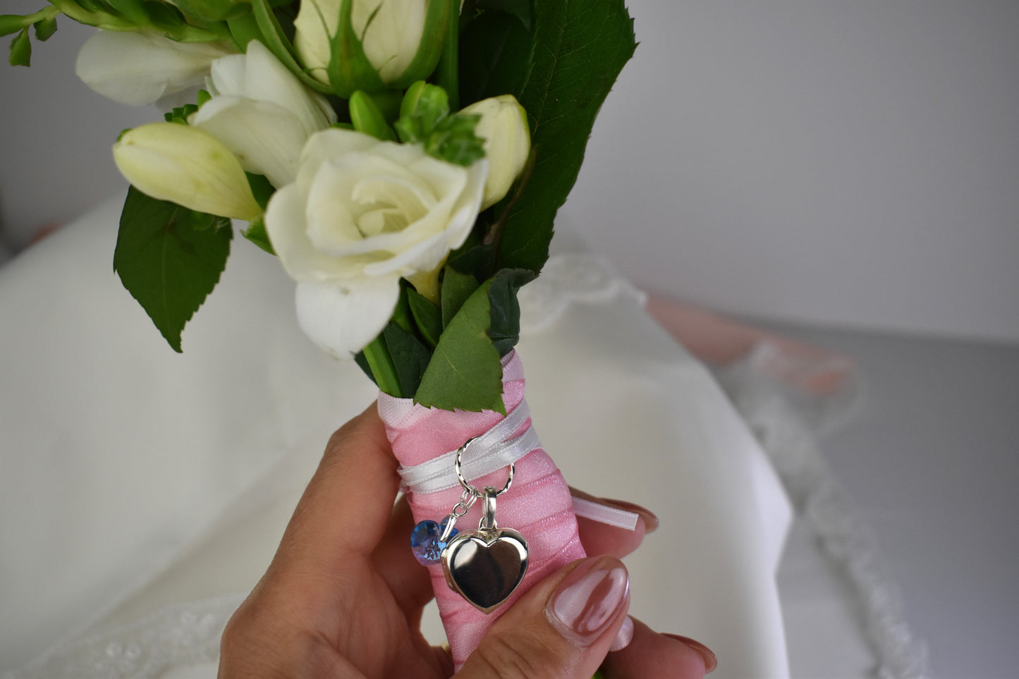 sterling silver heart shaped locket for two photos, accompanied by a blue crystal heart and threaded through a sterling silver loop. Ribbon supplied for you to attach to your bouquet. Easily detach the locket later to wear with a chain.