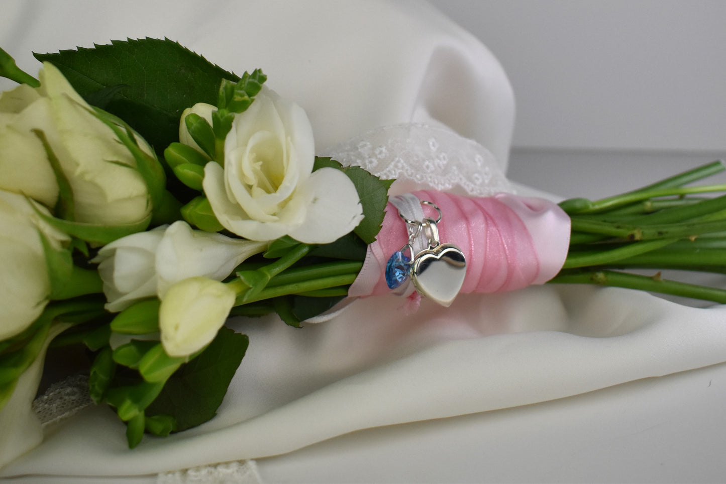 sterling silver heart shaped locket for two photos, accompanied by a blue crystal heart and threaded through a sterling silver loop. Ribbon supplied for you to attach to your bouquet. Easily detach the locket later to wear with a chain.