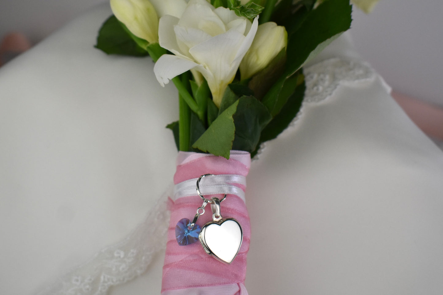 sterling silver heart shaped locket for two photos, accompanied by a blue crystal heart and threaded through a sterling silver loop. Ribbon supplied for you to attach to your bouquet. Easily detach the locket later to wear with a chain.