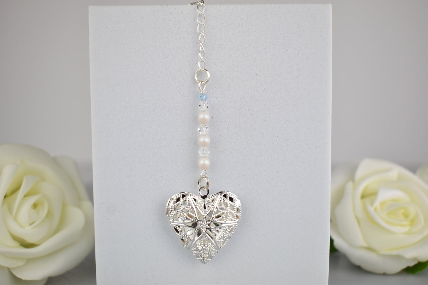Silver plated locket opens to take one photograph. Suspended from a line of high quality clear crystals and glass pearls. Topped with a tiny blue bead as a something blue. The chain has a lobster clasp at the end so that the clasp can be secured to a stem or fastened onto several stems via a loop inthe chain.