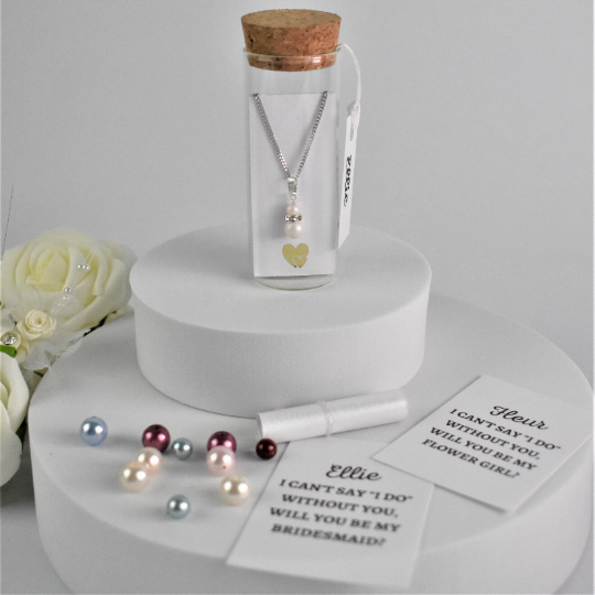 Double pearl drop pendant on silver chain is contained within a glass bottle with a scroll bridesmaid request. Bottle is finished with label showing bridesmaid's name