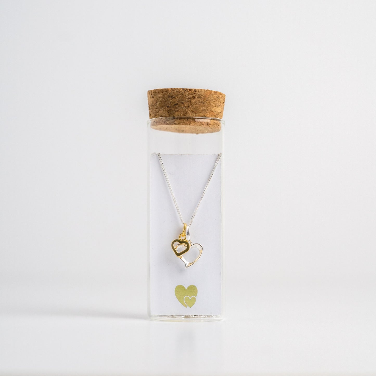 Message in a Bottle jewellery. A sterling silver heart is twinned with a smaller gold vermeil heart and suspended from a 16-18" sterling silver chain. The necklace is placed in a small glass bottle that includes a scroll for you to write your own message.