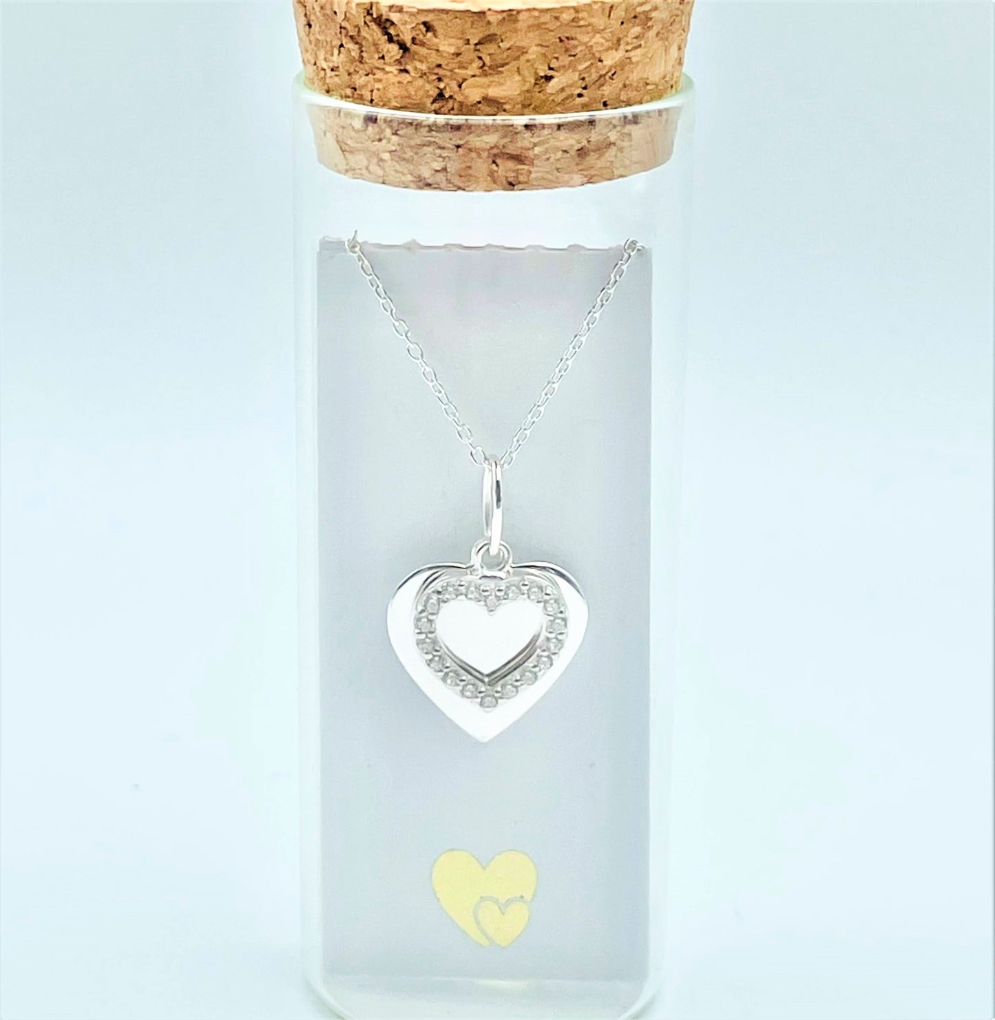 A sterling silver solid heart sits behind an outline zircona heart in a glass bottle. Behind the pendant is a scroll for you to add your own personal message. Presented in a cute glass bottle with a cork lid.