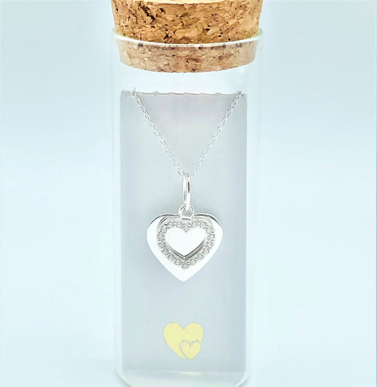 A sterling silver solid heart sits behind an outline zircona heart in a glass bottle. Behind the pendant is a scroll for you to add your own personal message.  Presented in a cute glass bottle with a cork lid.