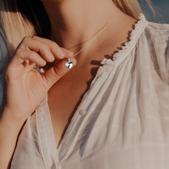Sterling silver heart shaped locket engraved with the word "Mum" in script and flower decoration. Suspended from a sterling silver chain, shown when worn/