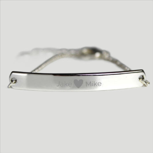 Silver colour bracelet shown with two personalised names etched on to front bar and separated by a small  etched heart.