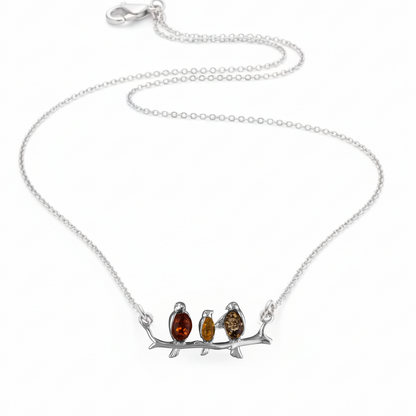 Sterling silver connector necklace showing three birds on a branch. The birds are inlaid with three types of amber - honey, cognac and olive. 