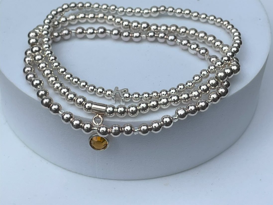 Silver plated beads surround a sterling silver hanger and birthstone of your choice. Shown with our silver bead bracelet and sterling silver initial bracelet.