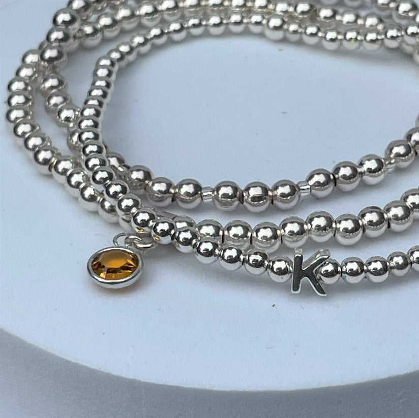 Close up of birthstone bracelet with silver beaded bracelet and sterling silver initial bracelet.