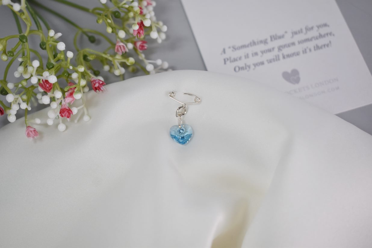 The secret something blue pin shown in sterling silver with high quality austrian crystal. A card showing the accompanying rhyme is shown in the background.