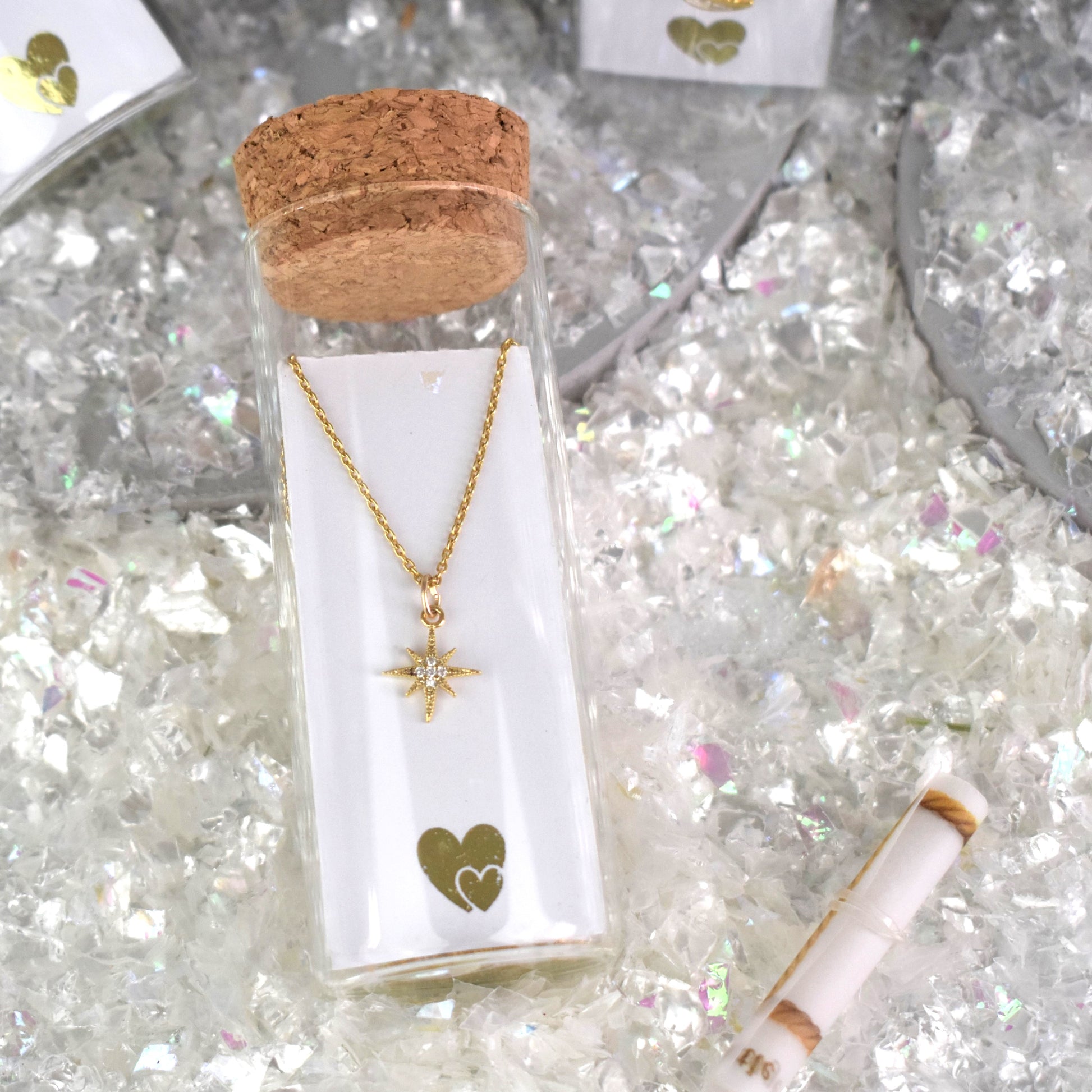 A pretty celestial star hangs from a gold vermeil chain and is placed in a glass bottle with a cork top. Behind the card is a scroll for your to add your own message in a bottle.