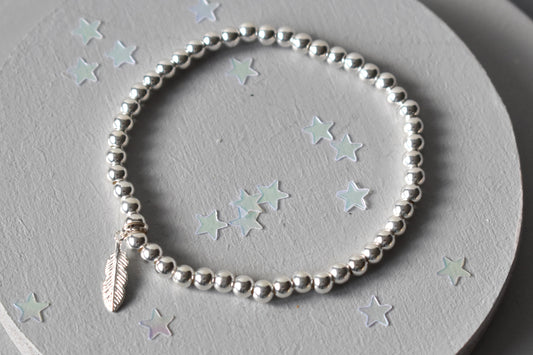Beaded bracelet consisting of 4mm sterling silver beads  threaded on strong elastic from which is suspened a sterling silver feather charm