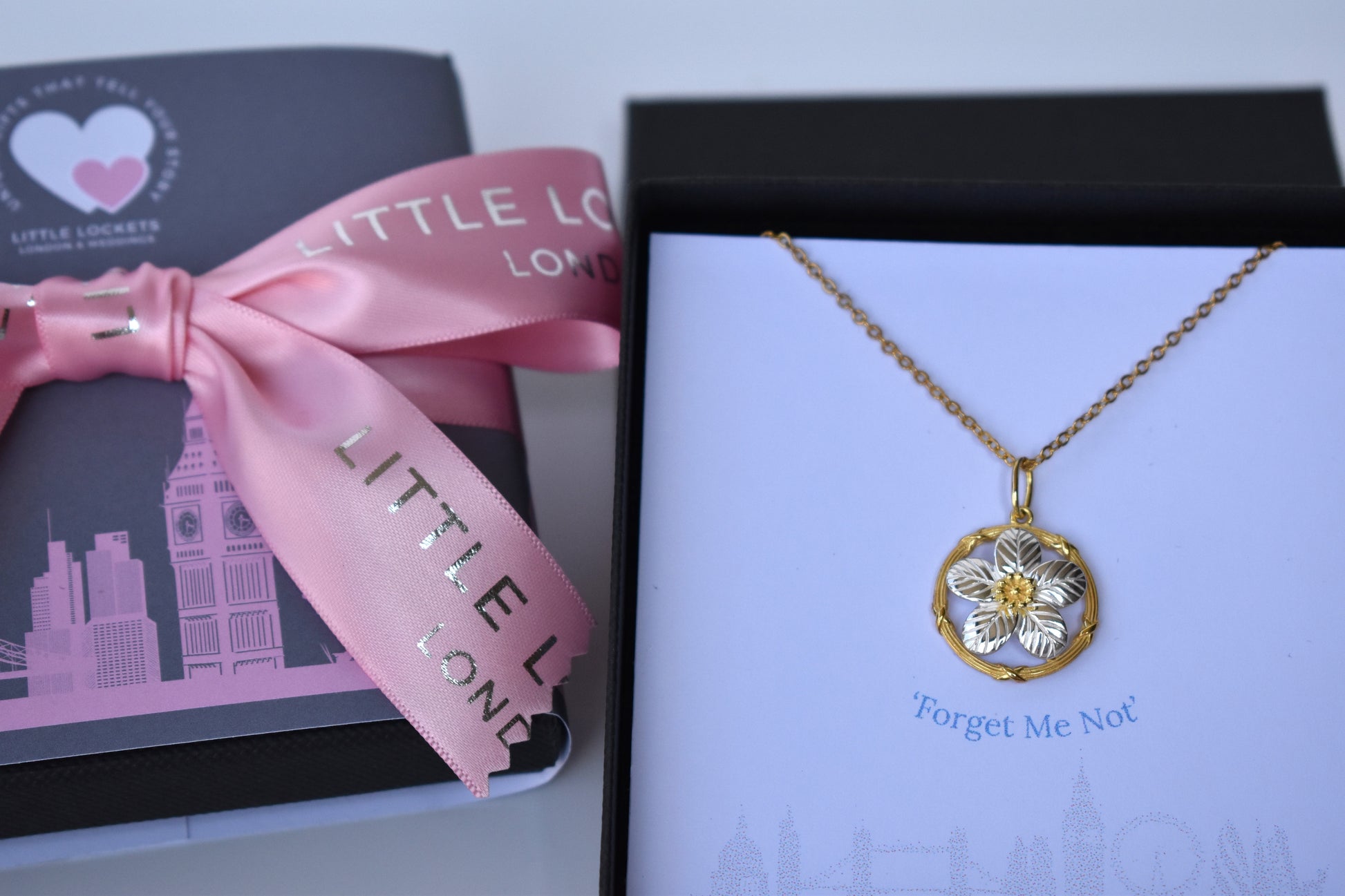 Sterling silver and gold plated forget me not pendant.  A delicate forget me not with sterling silver petals encased within a gold plated circle. Matching stud earrings. Necklace is shown in presentation gift box with the words "Forget me not" immediatlely underneath the pendant.