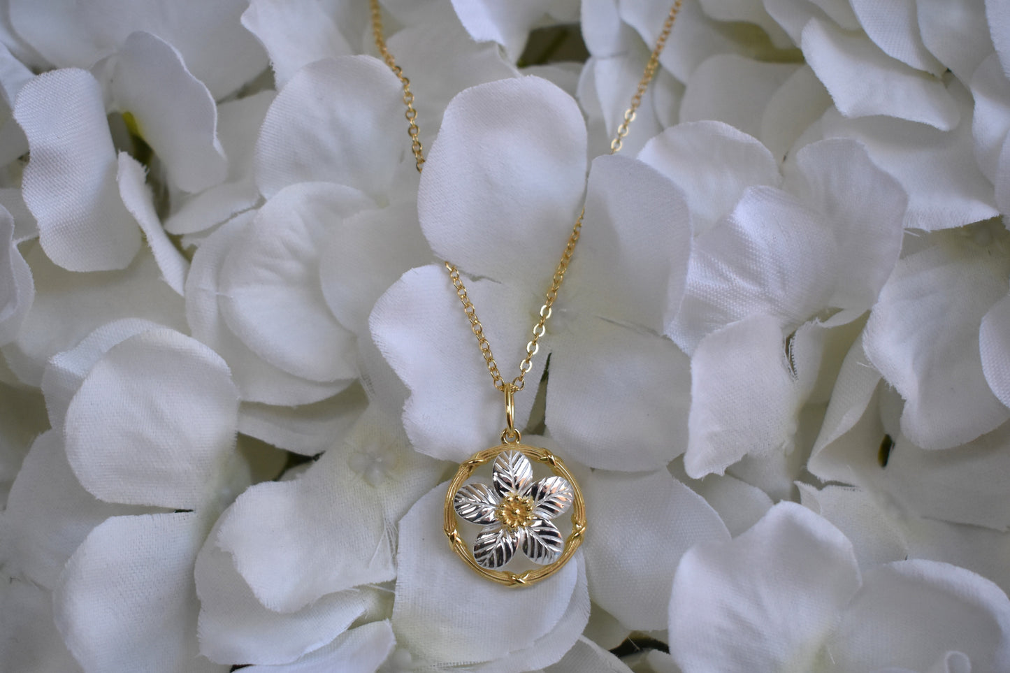 Sterling silver delicate forget me not flower with gold plated centre and circle surround. Suspended from a gold plated chain.