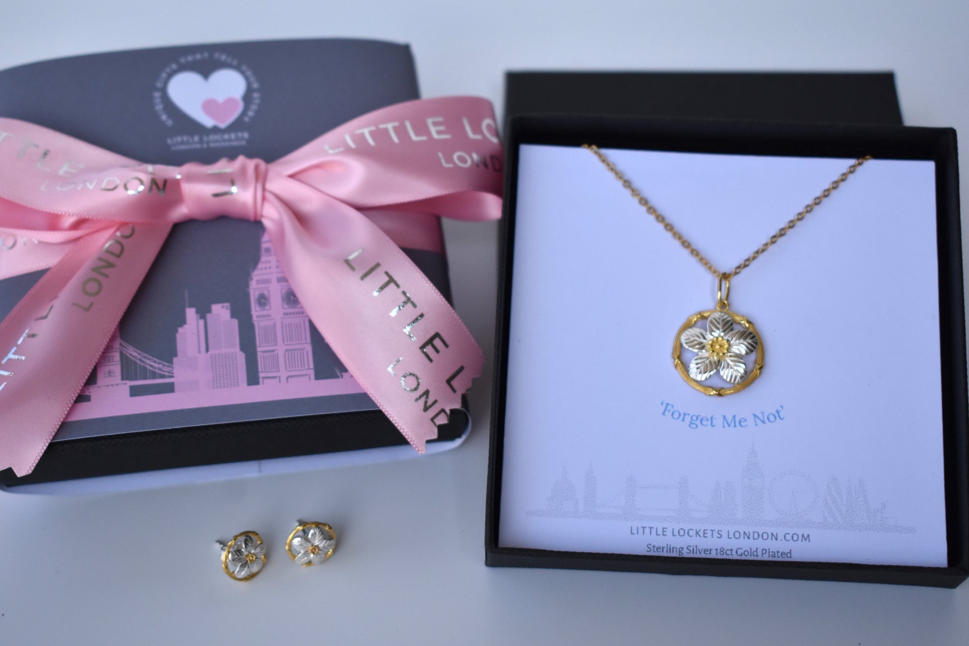 Sterling silver forget me not pendant with gold plated centre and surrounding circle. Presented in a branded gift box with the words "Forget Me Not" placed immediately underneath the pendant. Shown with option London wrap and ribbon tie.