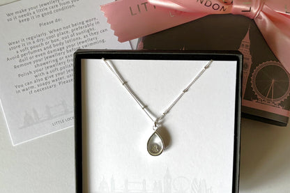 Glass pear-shaped opening locket in sterling silver and single crystal silver heart enclosed. Shown in gift box.