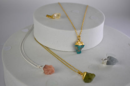 a selection of raw crystal pendants - pink opal, citrine, turquoise, moonstone, peridot