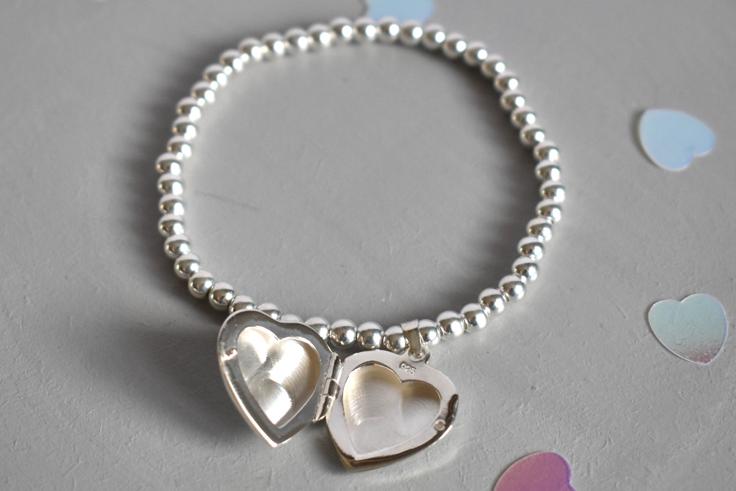 16mm heart shaped sterling silver locket suspended from 4mm sterling silver beads threaded onto strong elastic. The locket opens for you to add two photos of your choice. Shown open