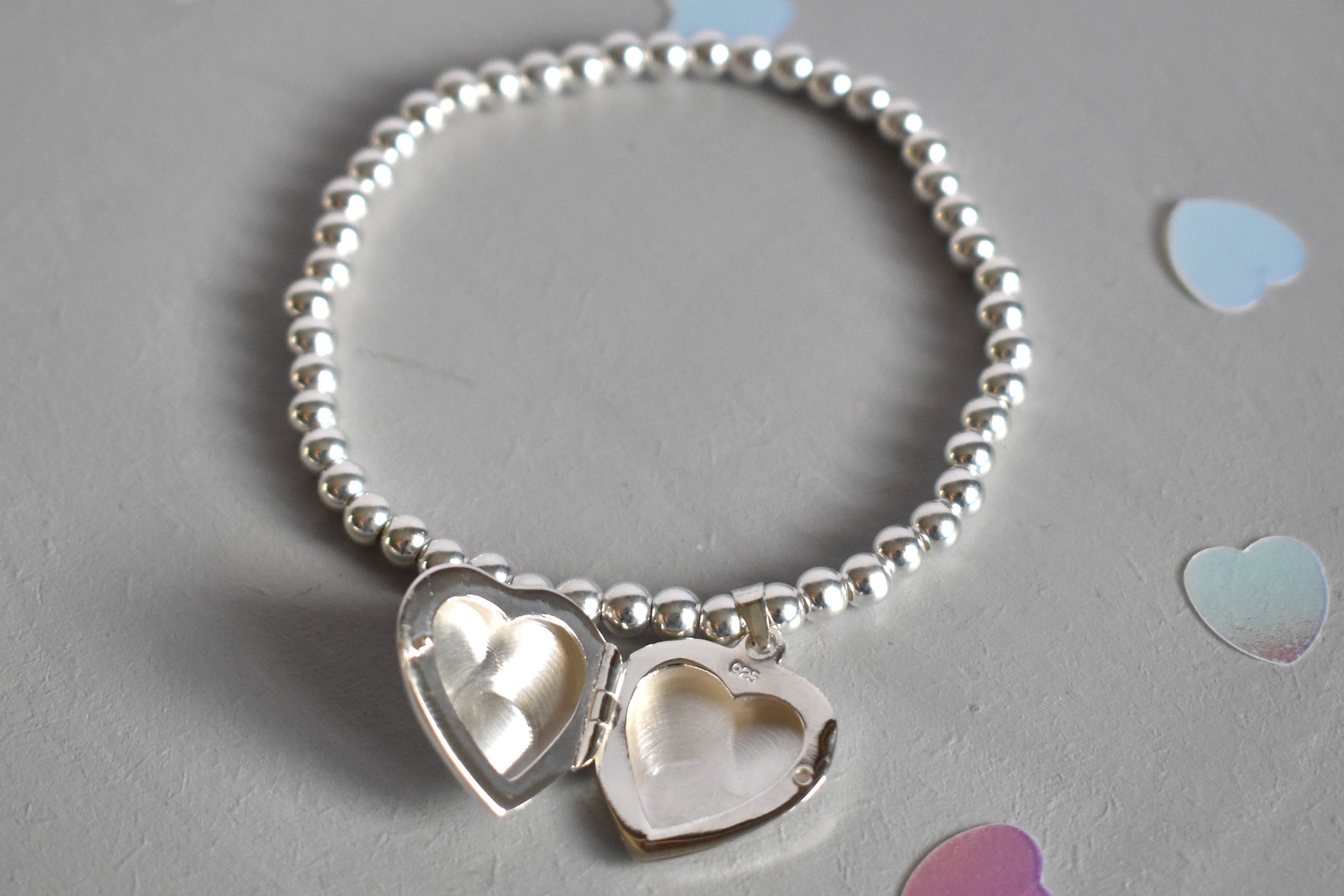 16mm heart shaped sterling silver locket suspended from 4mm sterling silver beads threaded onto strong elastic. The locket opens for you to add two photos of your choice. Shown open