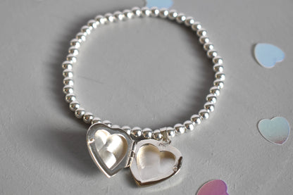 16mm heart shaped sterling silver locket suspended from 4mm sterling silver beads threaded onto strong elastic. The locket opens for you to add two photos of your choice. Shown open