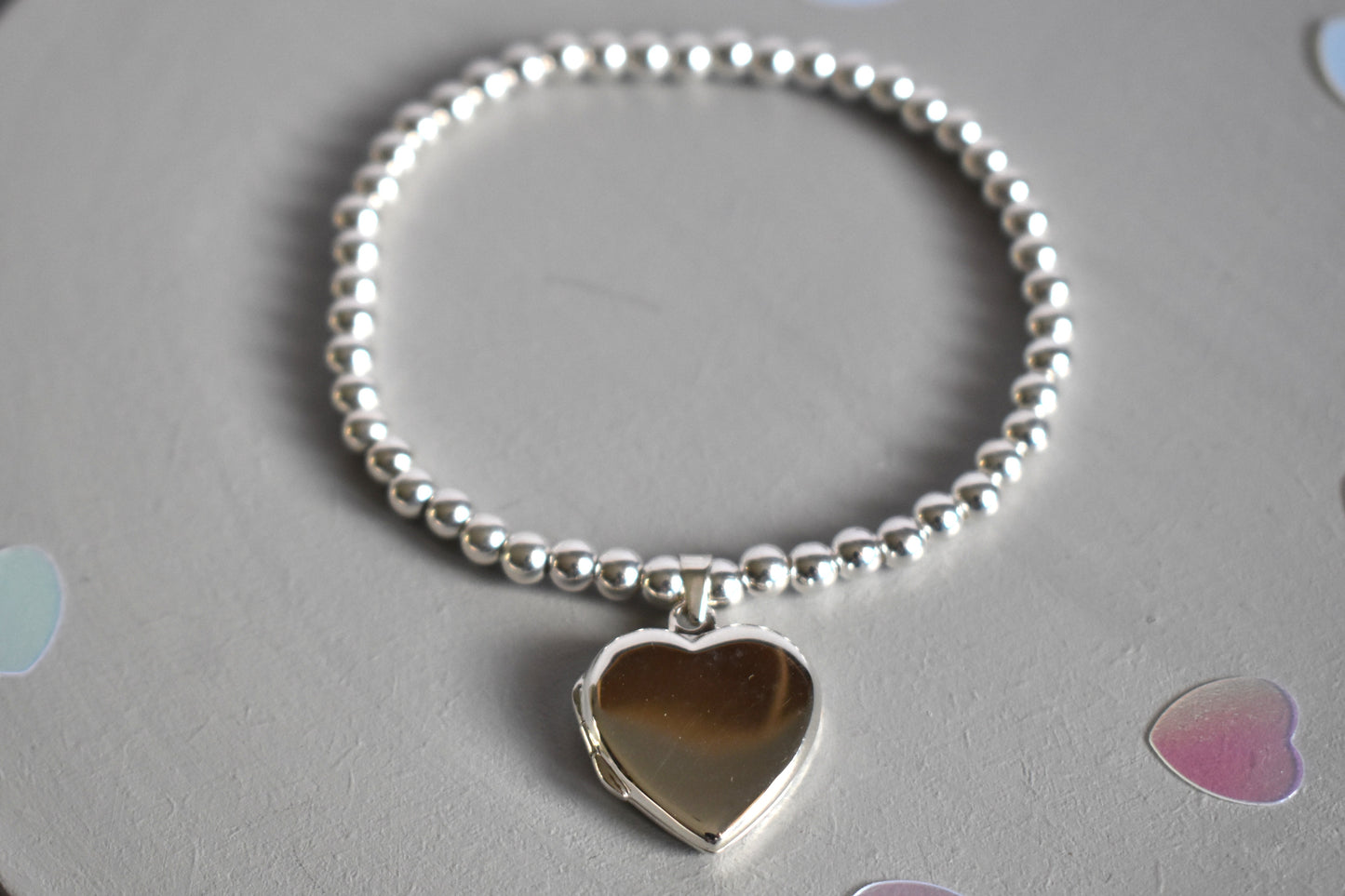 16mm heart shaped sterling silver locket suspended from 4mm sterling silver beads threaded onto strong elastic. The locket opens for you to add two photos of your choice.