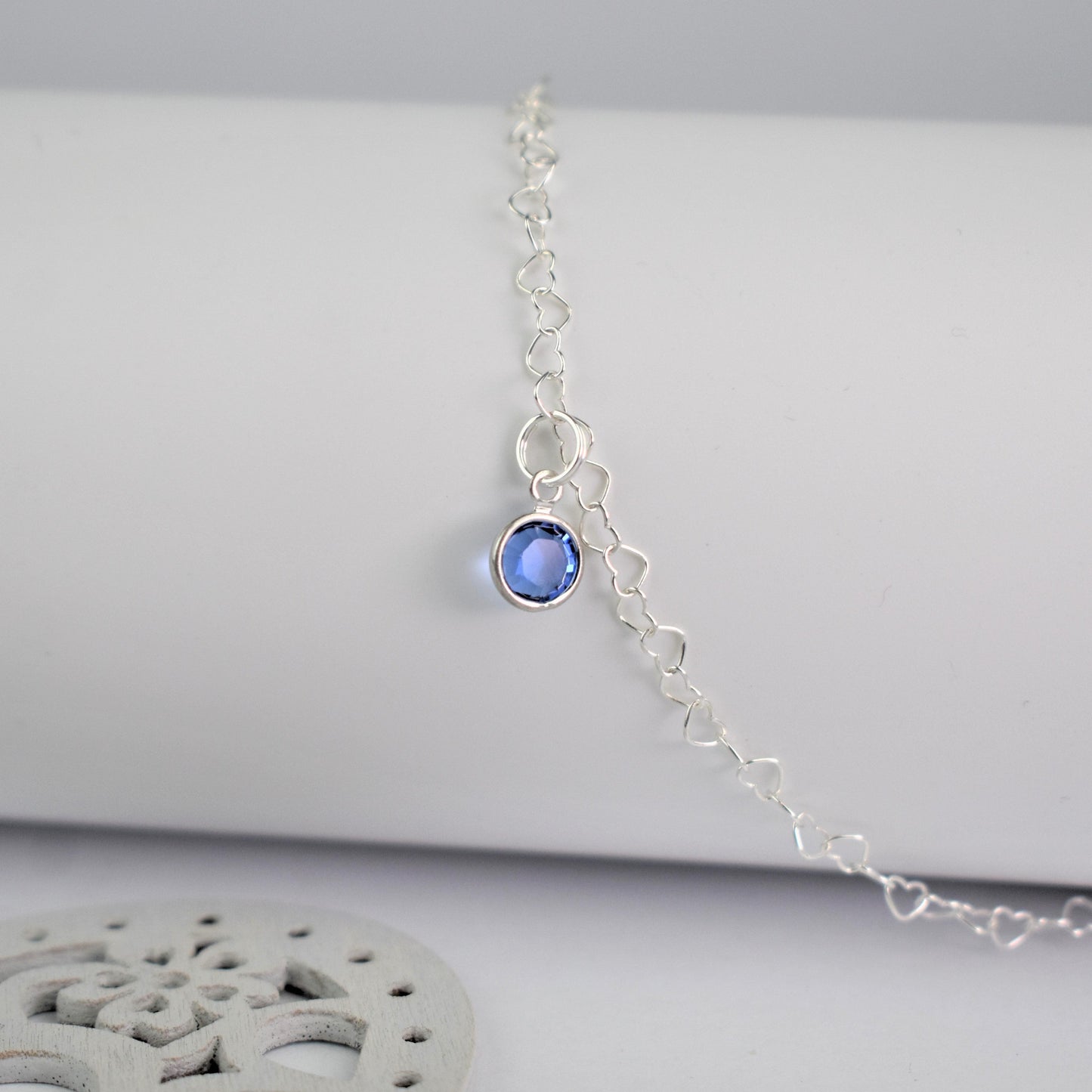 Sterling silver heart shaped links form this pretty anklet hung with a tiny blue crystal. Shown close up with link detail.