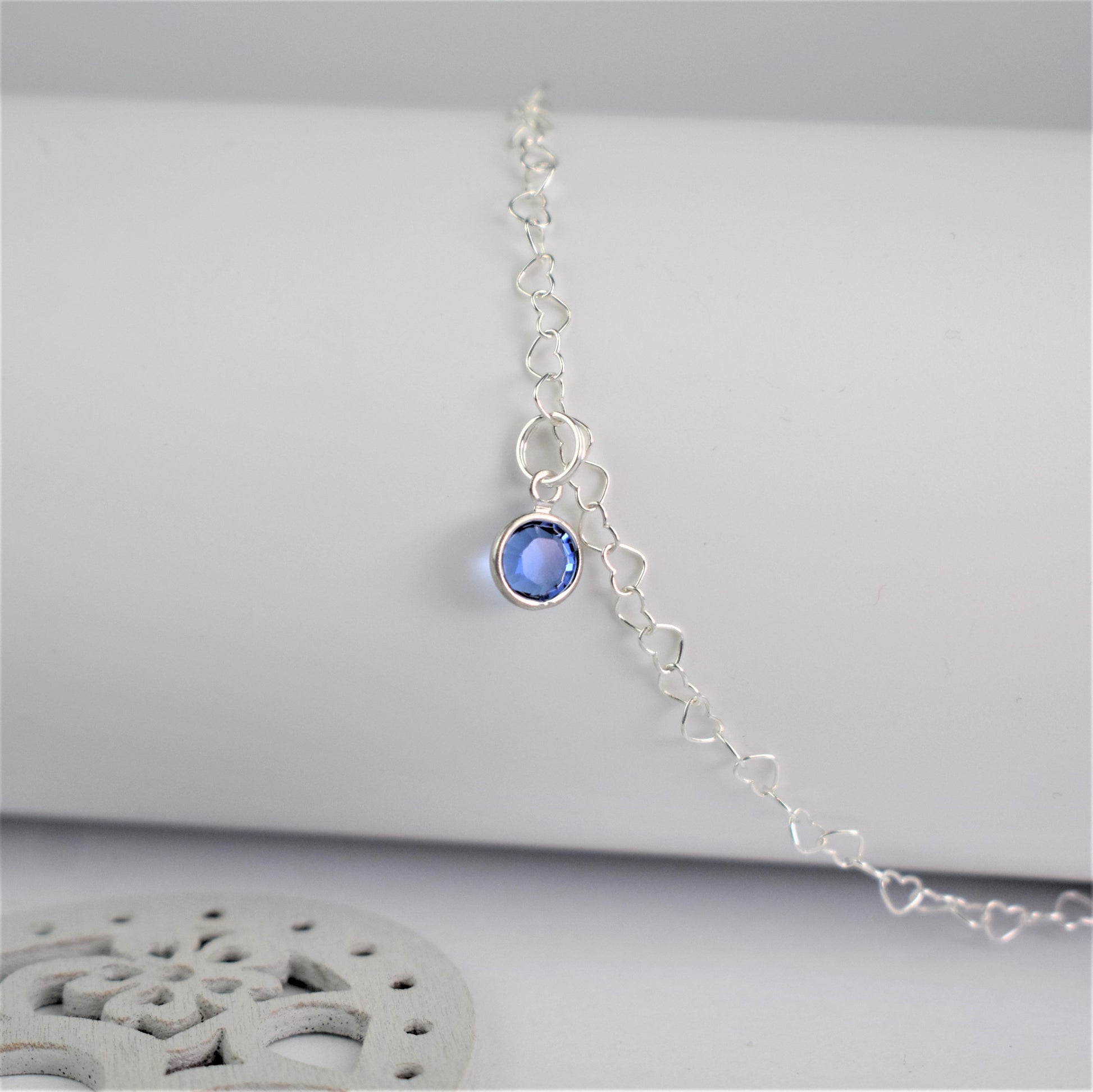 Sterling silver heart shaped links form this pretty anklet hung with a tiny blue crystal. Shown close up with link detail.