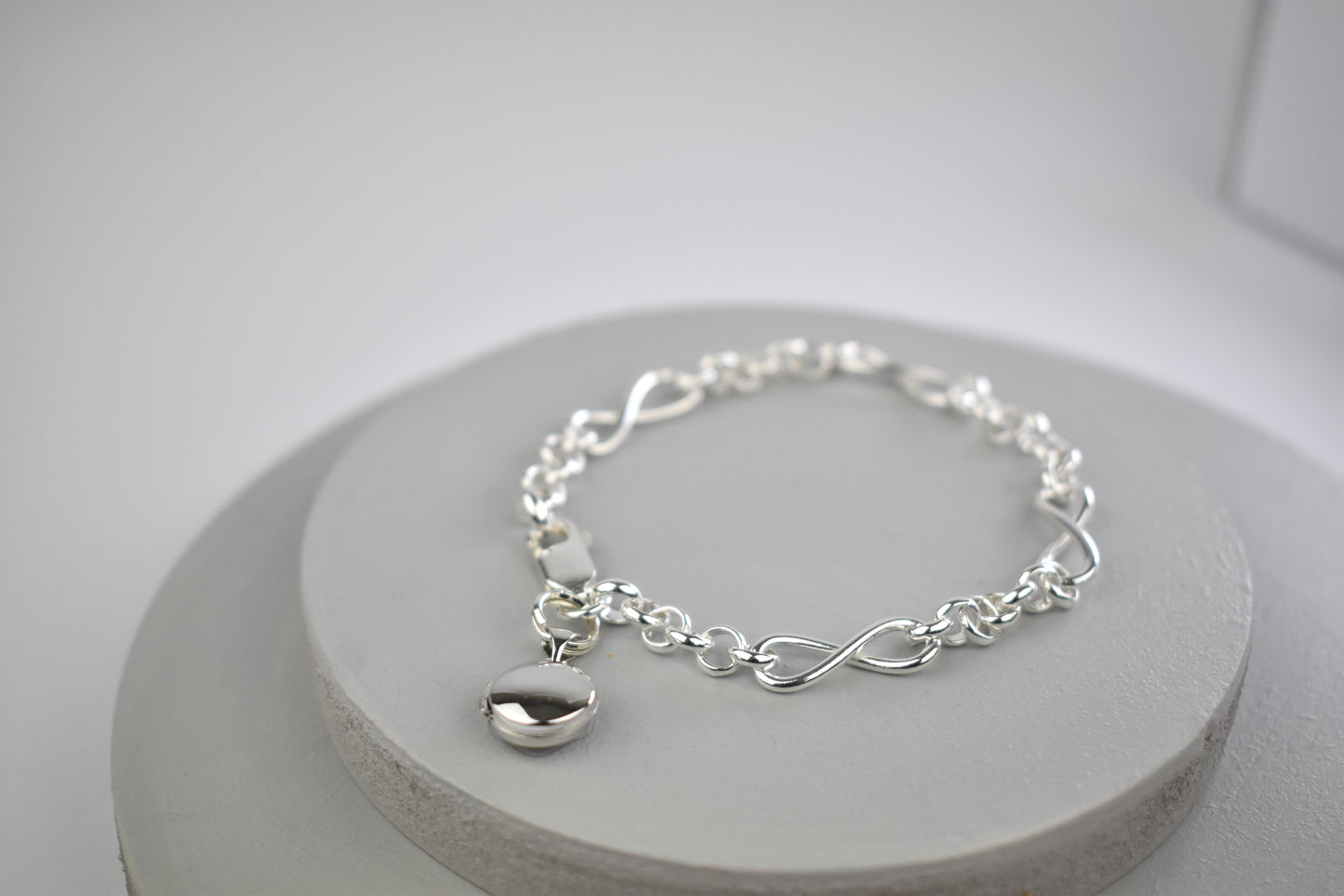 Sterling silver bracelet interspersed with three sterling silver infinity charms and with a tiny opening locket for you to add the photo of your choice. 