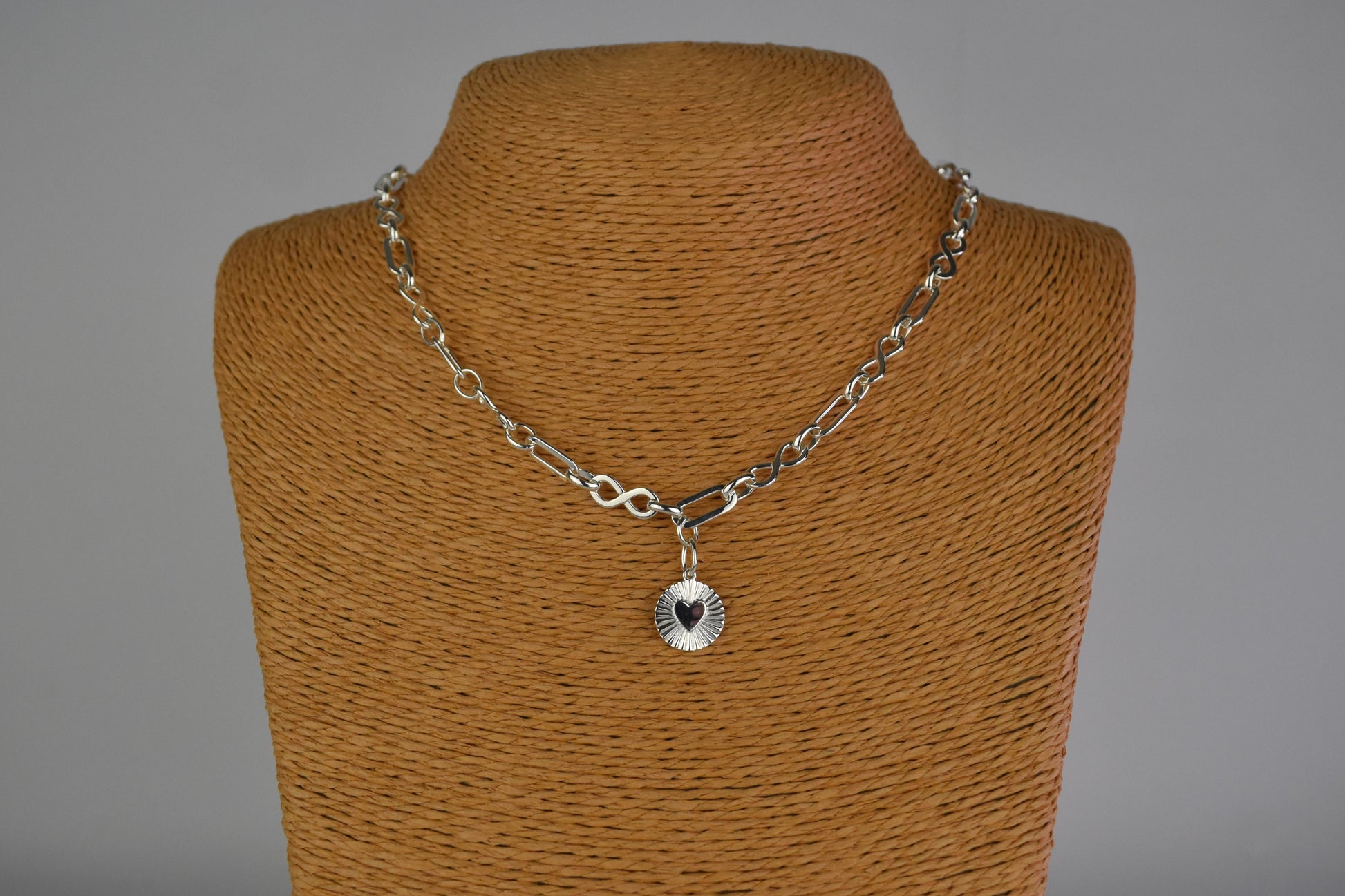 Sterling Silver Handmade Flat Link Infinity Necklace featuring a Heart Rays Pendant. Showcases flat oval and infinity links and features a Sterling Silver Sunburst Heart Rays charm pendant surrounded by an intricate sun rays design