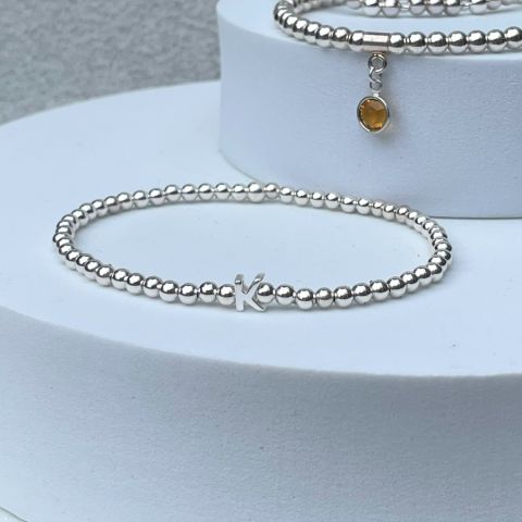 silver plated beads are interspersed with a single sterling silver slider initial and threaded onto strong elastic to make this stunning initial stacker bracelet.