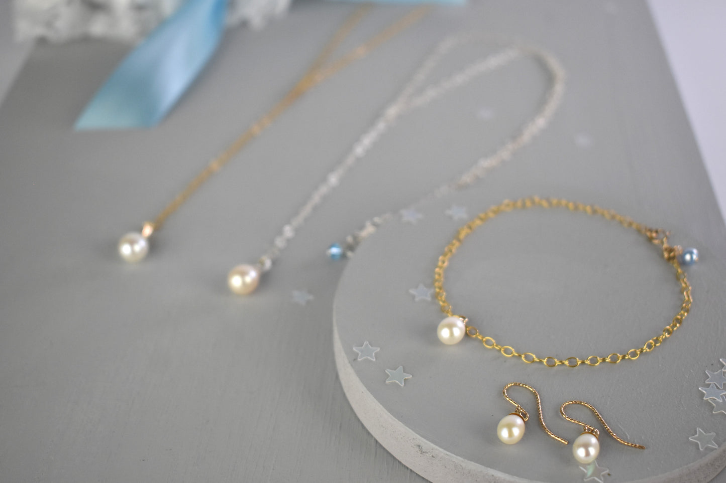 Something blue gift set shown in gold filled finish with sterling silver version in background. Freshwater pearls. on a lariat necklace, chain bracelet both finished with a tiny blue crystal or pearl. Matching freshwater pearl earrings on gold plated wires.