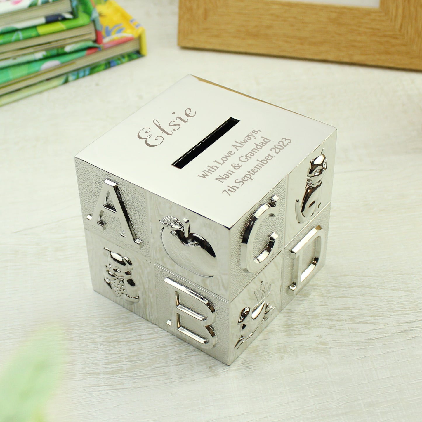 silver plated child's ABC money box. The child's name is engraved above the money slot in a script font. Beneath the money slot, there is room for three lines of text for your own message. 