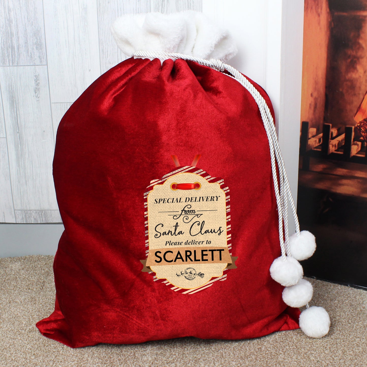 Christmas sack in red velvet with white furry trim, fastened with a twist cord finished with white pompoms. The sack has a printed "Special delivery from Santa Claus" tag the line "please deliver to" and room for a child's name.