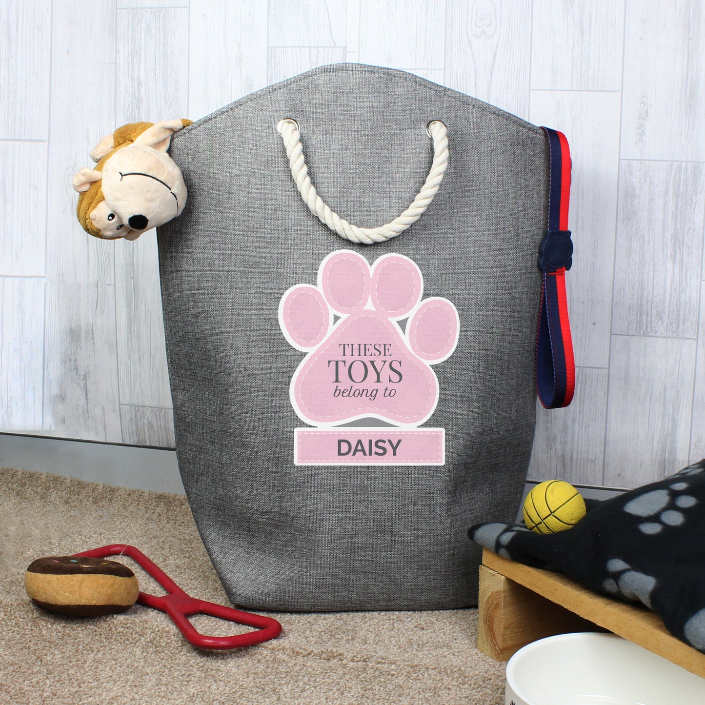 Robust Polyester pet toy bag in grey with choice of pink or blue paw print. Sturdy rope handles and a solid base make it easy to store all your pet's toys. Personalised iwth your pet's name. Shown with pink pawprint.