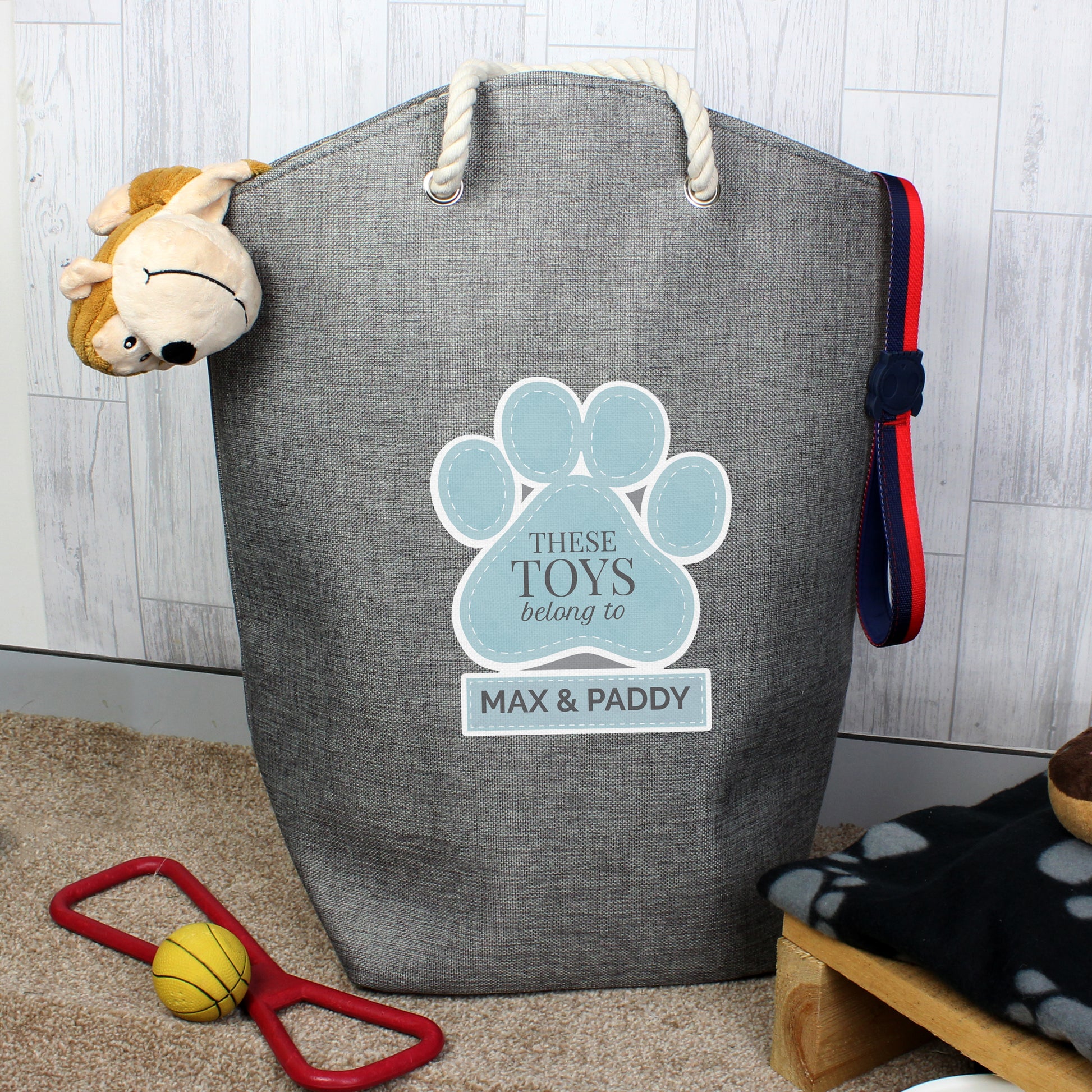 Robust Polyester pet toy bag in grey with choice of pink or blue paw print. Sturdy rope handles and a solid base make it easy to store all your pet's toys. Personalised iwth your pet's name. Shown with blue pawprint and two names (max 12 characters including spaces)