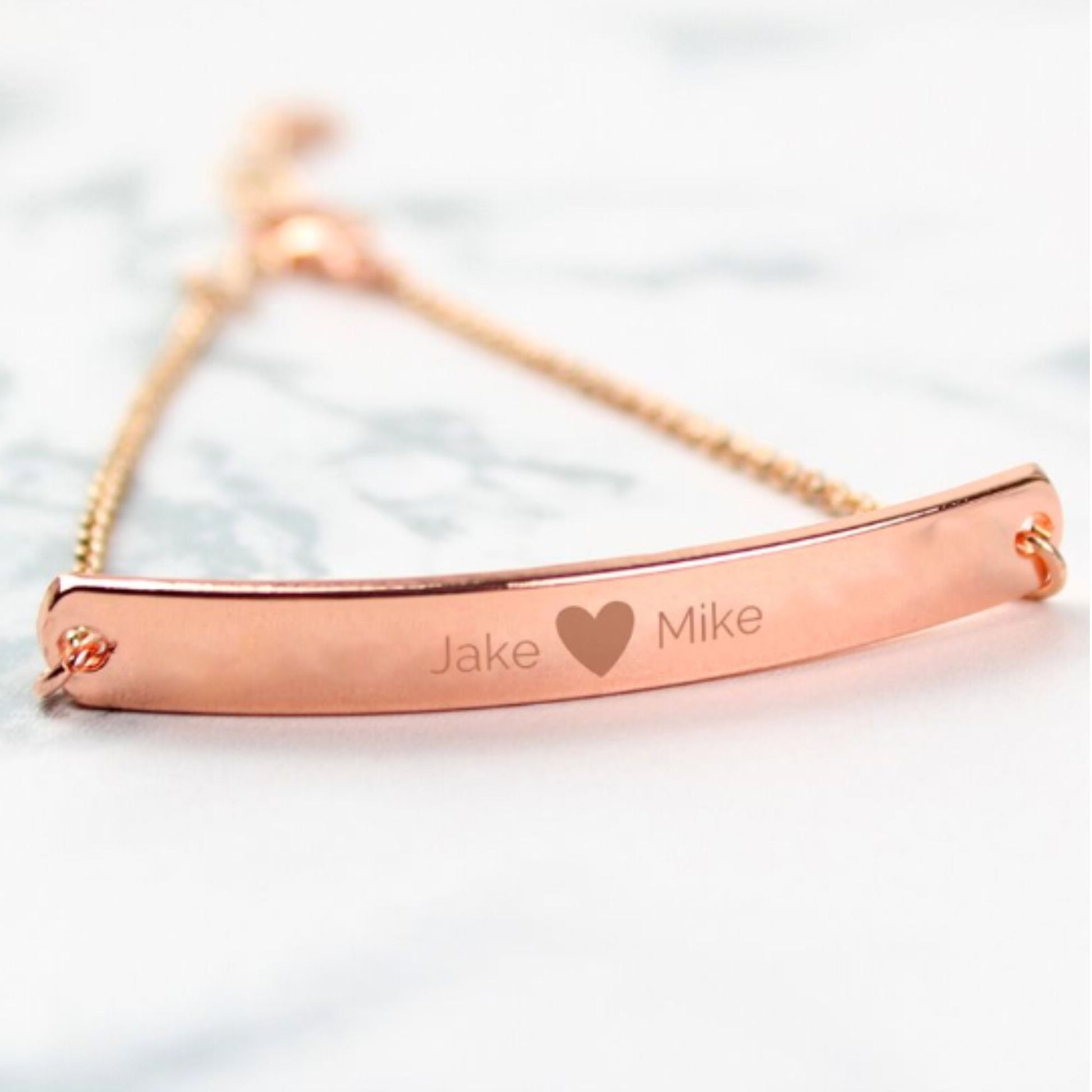 Rose gold colour bracelet shown with two personalised names etched on to front bar and separated by a small etched heart.