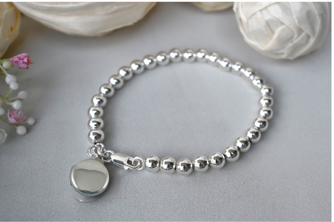 Sterling silver beaded bracelet with a lobster clasp. Next to the clasp is an round plain sterling silver locket 