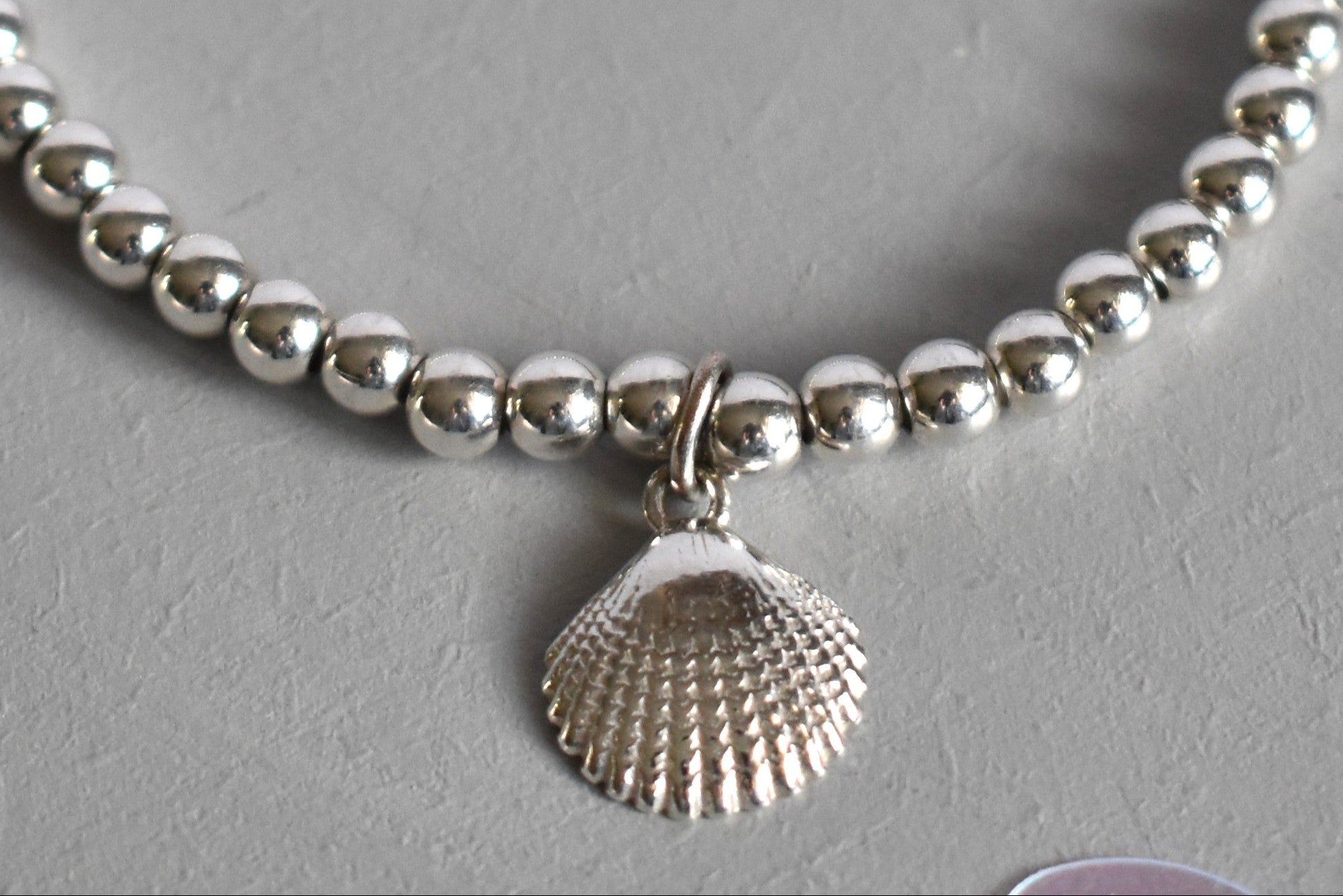 Close up of Sterling silver beaded bracelets with 4mm beads. Suspended from the bracelet  is a sterling silver clamshell. From the Ocean Collection of stacking bracelets.